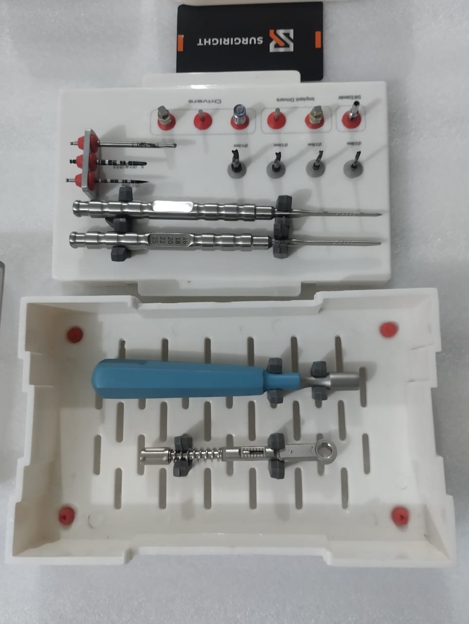 Compact dental implant driver set and drill extenders organized in a autoclavable white surgical cassette box by SurgiRight
